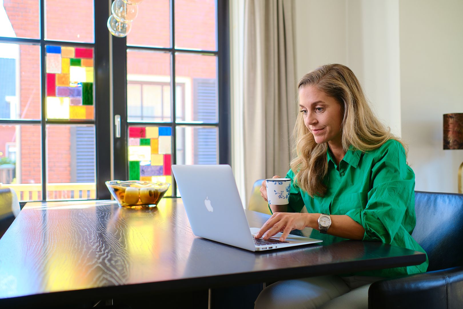 Een vrouw die achter haar laptop zit met een kopje in haar hand